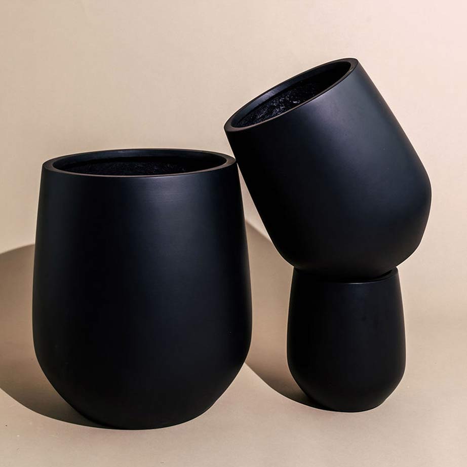 Black garden pots in three different sizes with the medium sized pot balanced on top of a small pot.
