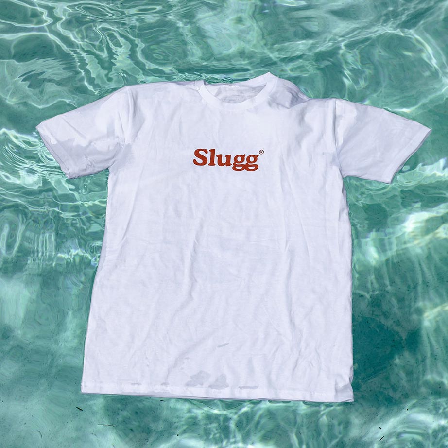 A white t-shirt that says "Slugg" in burnt orange writing floats in a sparkling aqua swimming pool