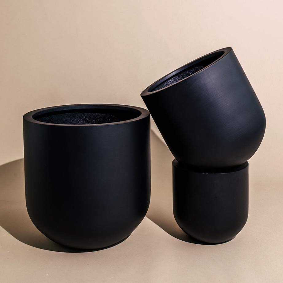 Two stacked black garden pots leaning against a larger sized black garden pot.