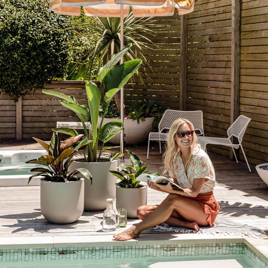 A happy plant enthusiast relaxes beside her Thomas garden pots while reading a design magazine in the sunshine. 